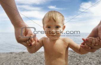portrait of a baby boy holding his father's hands on beach backg