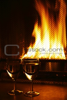 two wine glasses against fireplace with flame in dark light