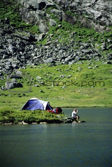 Young across lake sitting next to camp