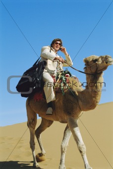 Man with mobile phone riding camel in desert