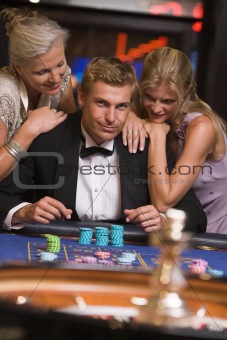Man gambling in casino surrounded by attractive women