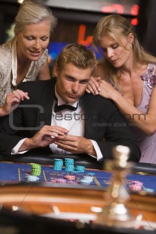 Man gambling at casino surrounded by glamorous women