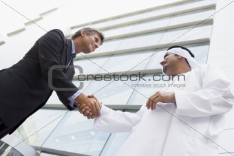 A Middle Eastern businessman and Caucasian man shaking hands out