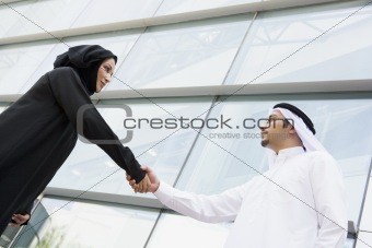 A Middle Eastern businessman and woman shaking hands outside an 