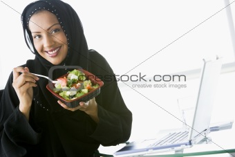 A Middle Eastern businesswoman eating salad beside her laptop