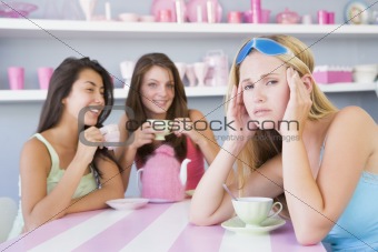 Two young women enjoying a tea party while one sits apart wearin