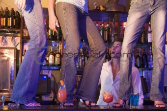 Barman gaping at three young women dancing on bar counter 