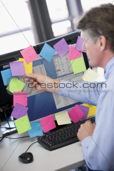 Businessman in office at monitor with notes on it
