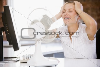 Businesswoman in office with computer and fan cooling off