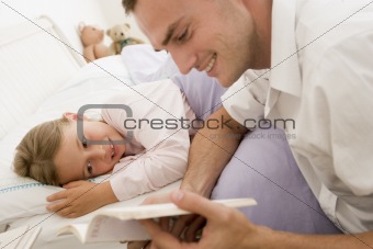 Man reading book to young girl in bed smiling