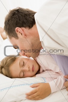 Man waking young girl in bed with kiss