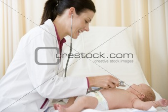 Doctor giving checkup with stethoscope to baby in exam room smil