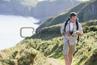 Man walking on cliffside path looking at map