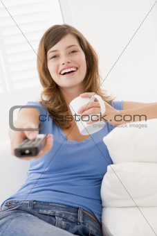 Woman in living room with remote control and coffee smiling