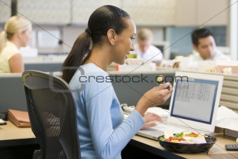 Businesswoman in cubicle eating sushi smiling