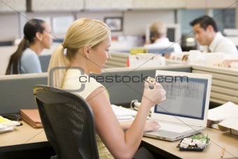 Businesswoman in cubicle using laptop eating sushi
