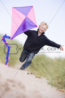 Young boy running on beach with kite smiling