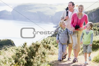 Family walking on cliffside path holding hands and smiling