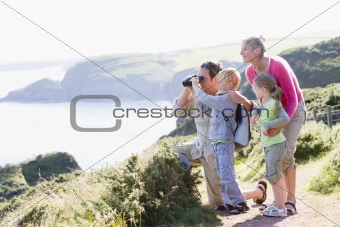 Family on cliffside path using binoculars and smiling