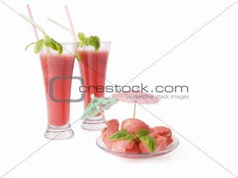 Two glasses of a water-melon drink (smoothie) and a water-melon cut out by balls and decorated with leaflets of mint and umbrellas. Isolated on a white background.