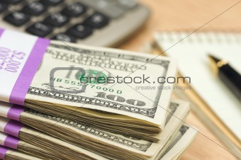 Stack of Money, Calculator, Pad of Paper and Pen with Narrow Depth of Field.