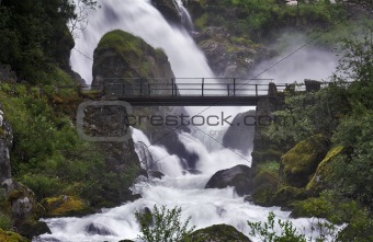 Bridge across the stream near a powerful waterfall 