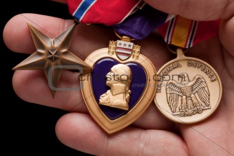 Man Holding Purple Heart, Bronze and National Defense War Medals in The Palm of His Hand.