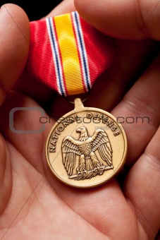 Man Holding National Defense War Medal in The Palm of His Hand.