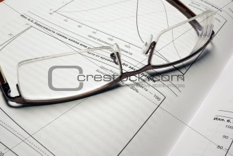 Glasses laying on book with financial charts.