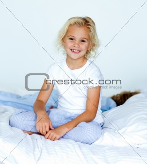 Little girl in bed smiling at the camera while her brother is sl