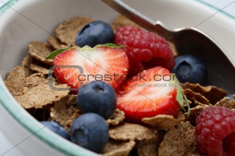 Bowl of breakfast cereal with fruit and a spoon.