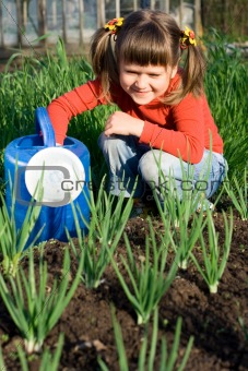 Smiling girl with watering can is sitting near onion patch 