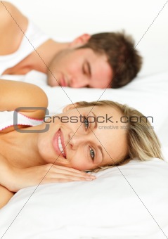 Couple lying in bed and woman smiling at the camera