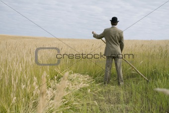A man mows a grass with a scythe