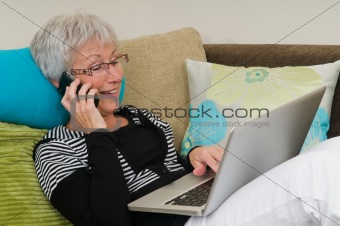 Senior woman working on a laptop, sitting relaxed on the couch.
