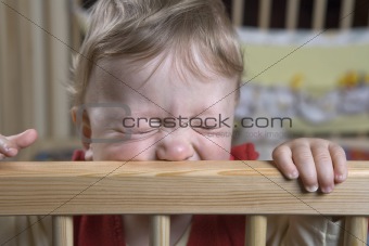 cute boy standing in the playpen holding on the fence