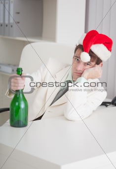 Young businessman in Christmas cap sits with bottle at table