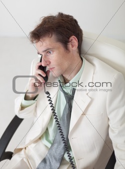 Man in white suit speaks by phone sitting in an armchair