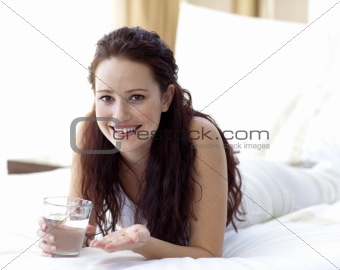 Woman in bed taking pills with water
