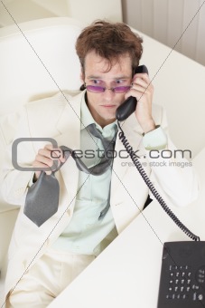 Young businessman speaks on phone, worries and rumples tie