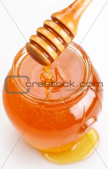 Full honey pot and spilled honey on a white background.