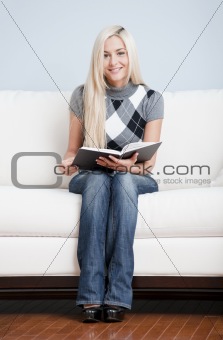 Young Woman Sitting on Sofa Holding Open Book