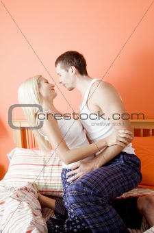 Young Couple Kneeling on Bed Embracing