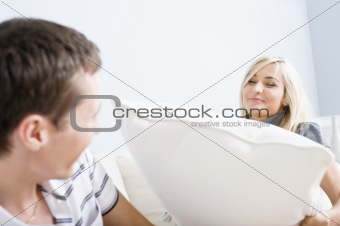 Young Woman Smiling and Hitting Young Man With Pillow