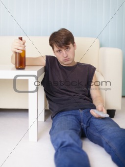 Drunk man sits on floor at TV with a bottle