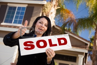 Happy Attractive Hispanic Woman with Thumbs Up Holding Sold Sign In Front of House.