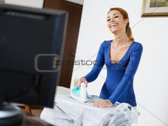 woman ironing shirt while watching television