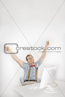 Young man happy with arms raised in front of computer.