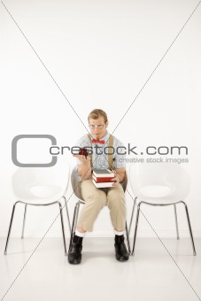 Young man sitting with books and holding out apple.