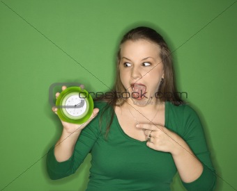 Young female Caucasian adult holding and pointing to clock.